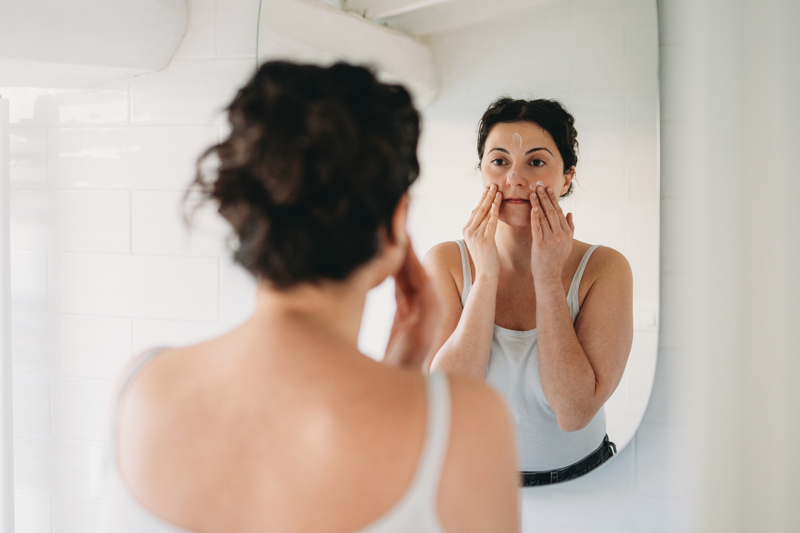 A woman looks in the mirror touching her skin