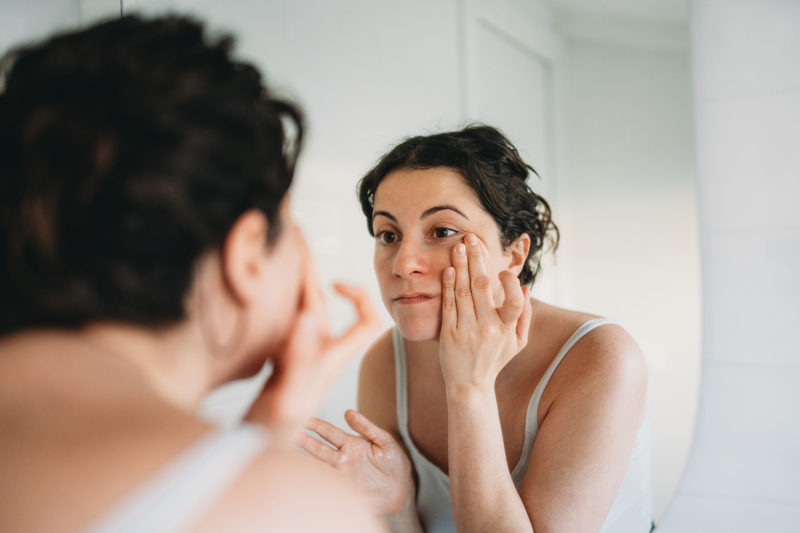 A woman looks at her face in the mirror